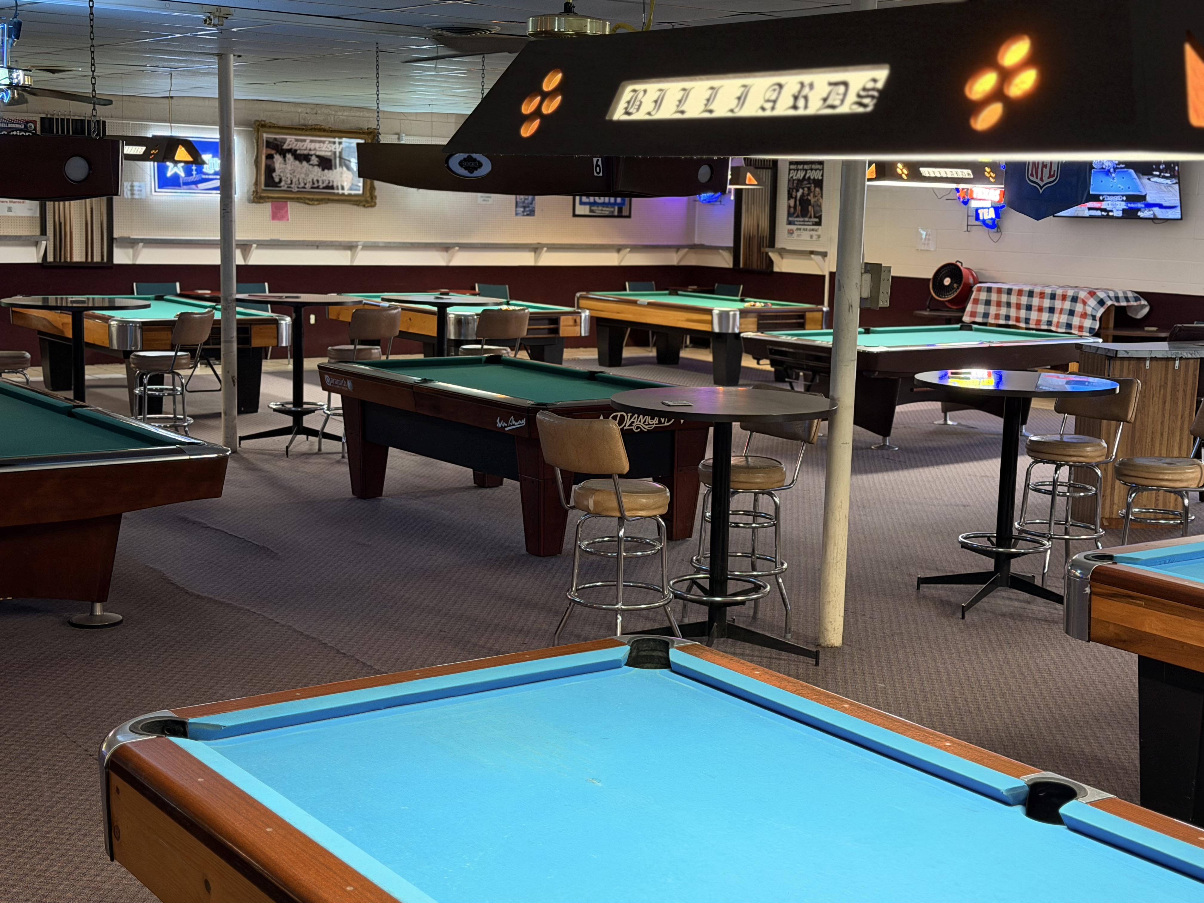 Rows of pool tables under classic Billiards light fixtures at Billiards Plus