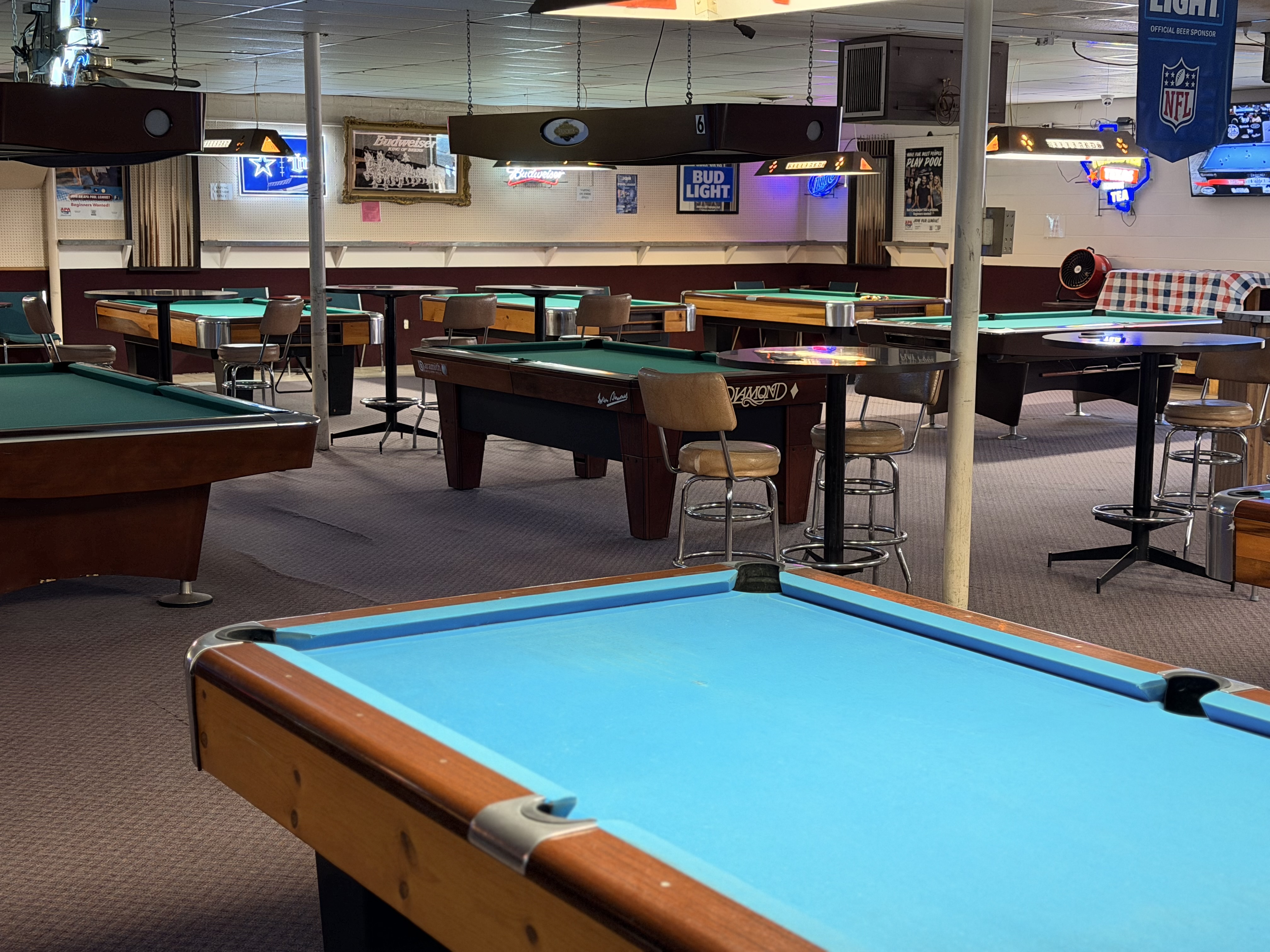 Wide view of the Billiards Plus room with many pool tables and high-top seating