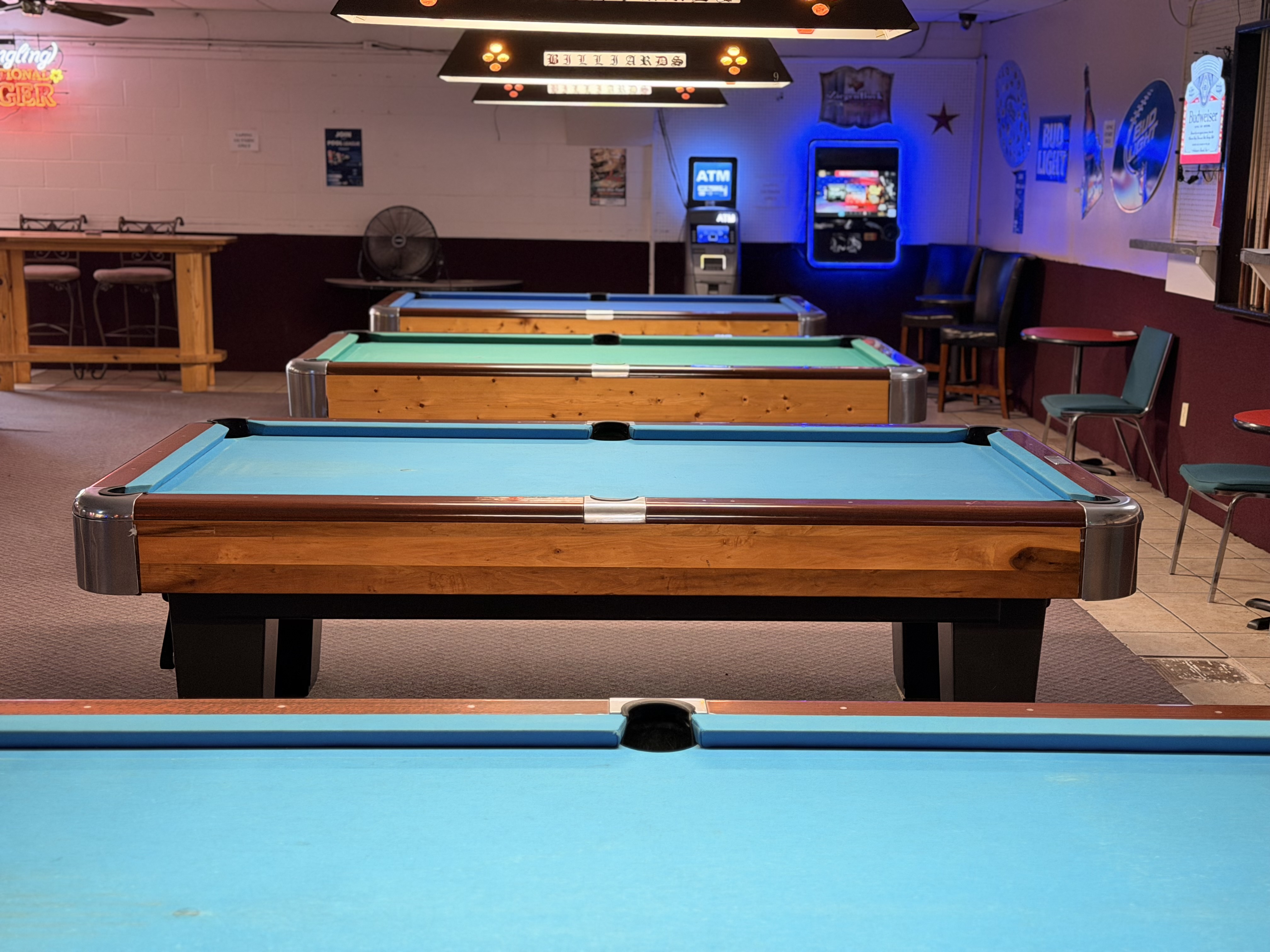 A row of pool tables with an ATM and neon beer signs in the background
